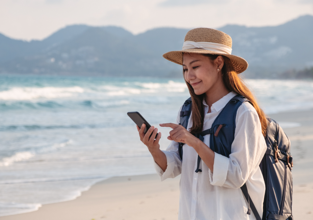 woman on a beach smiling and looking at her phone