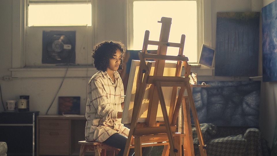Picture of a woman painting a picture in front of an easel.