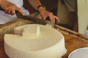 Raw cheese on a table being cut by a person.