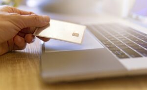Picture of a person holding a credit card above a laptop computer.