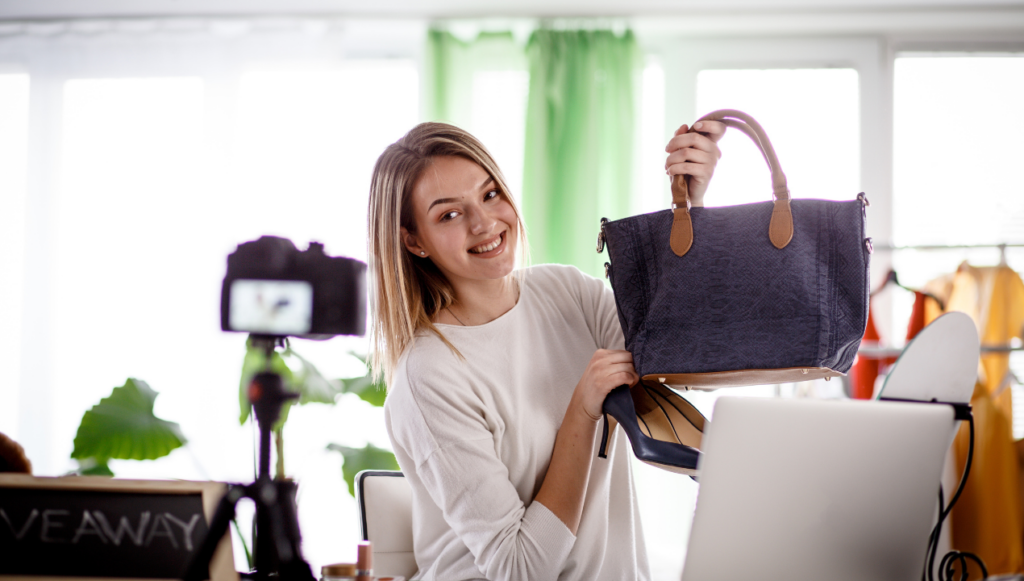 fashion blogging ideas - fashion blogger holding up a handbag in front of a camera