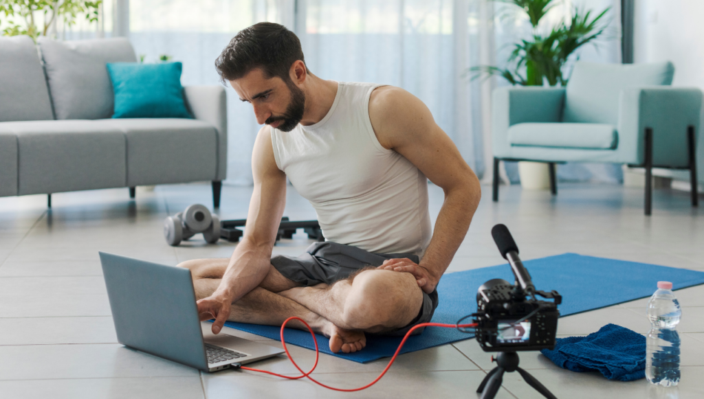 creative business ideas - a personal trainer sat on a yoga mat setting up a laptop and a camera