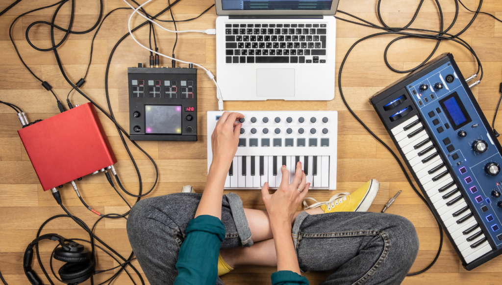 How to Sell Digital Downloads on Amazon - a person sat on the floor surrounded by musical keyboards, recording equipment and a laptop