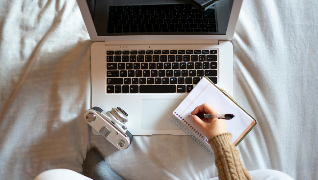 How to Sell Digital Downloads on Amazon - someone taking notes at a laptop with a camera next to them